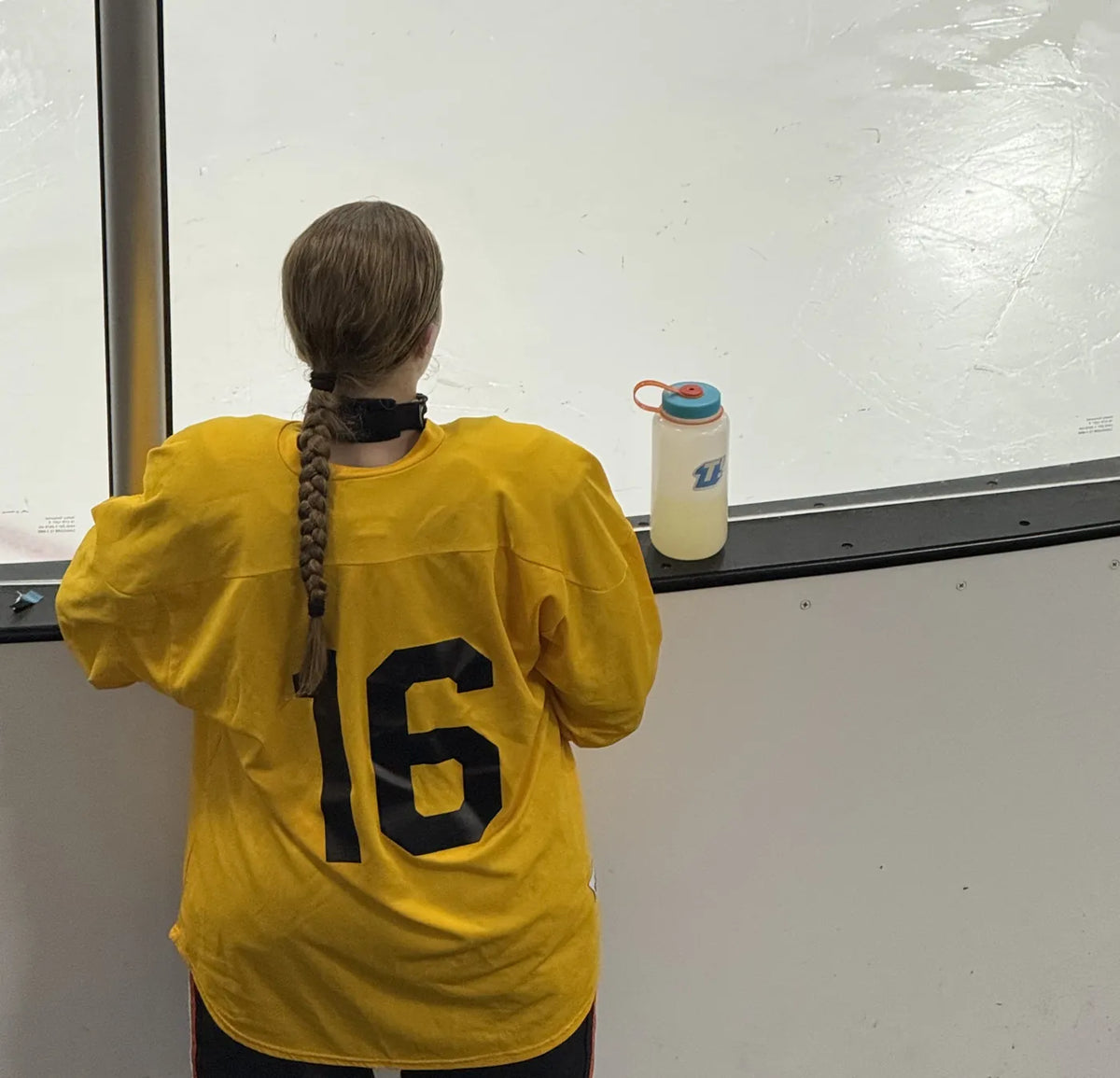 A young hockey player leaning on the rink boards with a Torrent bottle on the ledge